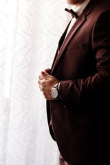 man in an elegant brown tuxedo with a silk bow tie and a watch. selective focus.