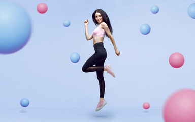 Fototapeta premium Amazing woman in trendy sportswear jumping. Smiling beautiful slim brunette young girl in fashion leggings and pink top expressing happy emotions. Blue background.