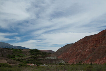Rural scenic. Panorama view of a small farm house, grassland and red sandstone hill under a beautiful sky with clouds.