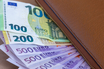 100, 200, 500 euro banknotes under a brown wallet, closeup



