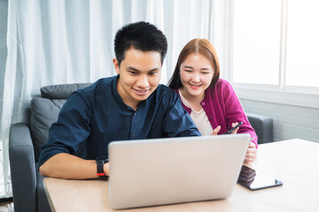 Asian couple online shopping ecommerce together from home modern living room using phone computer laptop tablet payment paying transaction money transfer credit debit card smiling happy joyfully