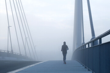 Joggerin läuft bei Nebel über eine Brücke 