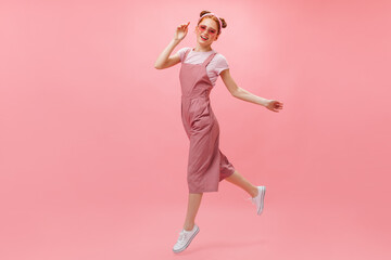 Active woman in pink jumpsuit, T-shirt and stylish glasses moves on pink background