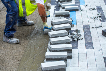 Construction work on pavement. Installation of concrete paver blocks on the sidewalk. The worker...
