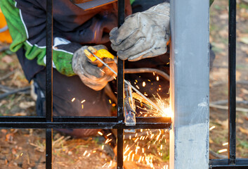 A worker welder works with metal, welds a metal fence in an autumn park.