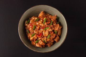 Kung Bao chicken on a black background. A Chinese dish with chicken, chili, peanuts, sauces and onions.