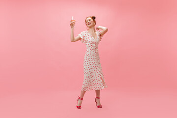 Cool girl in white dress with cherries inflates confetti on pink background