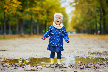 Child wearing yellow rain boots and jumping in puddle