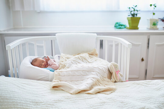 Newborn baby having a nap in co-sleeper crib attached to parents' bed
