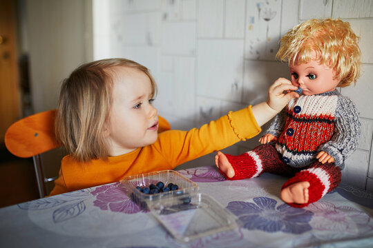 Adorable Toddler Girl Eating Blueberries And Feeding Her Doll