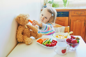 Adorable toddler girl eating fresh fruits and vegetables for lunch