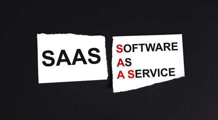 SaaS software as a service.TEXT ON WHITE PAPER ON BLACK BACKGROUND