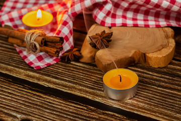 
Cinnamon sticks tied with a jute rope against the background of a red-white checkered tablecloth with several stars of anise on a wooden stand.