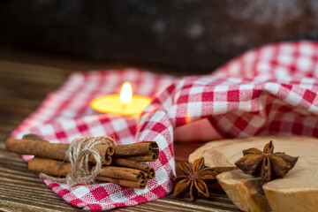 
Cinnamon sticks tied with a jute rope against the background of a red-white checkered tablecloth with several stars of anise on a wooden stand.