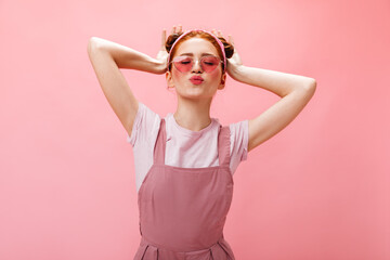 Optimistic girl in pink outfit and sunglasses posing with raised arms on isolated background