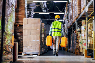 Worker in vest relocating cans with oil while walking in warehouse.
