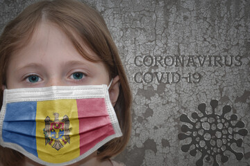 Little girl in medical mask with flag of moldova stands near the old vintage wall with text coronavirus, covid, and virus picture. Stop virus concept
