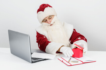 Santa Claus is sitting at his desk and wrapping a gift.