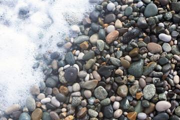 Wet smooth glossy sea shingle and white sea foam close up background in natural colors. Grey, white and brown tranquil palette.