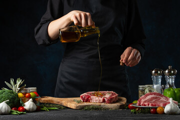 The chef in black apron pours oil on the fresh beef or pork steak on the wooden chopping board. Frozen motion. Backstage of cooking meat. Tasty food concept.