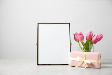 Fototapeta na wymiar Beautiful tulips, gift and blank photo frame on light table