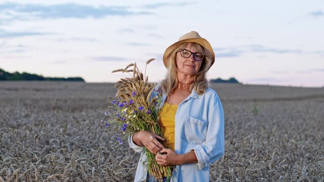 Romantic Image Of Woman With Bouquet On Background Of Sky. She Stands In The Middle Of Wheat Field With Spikelets And Flowers In Her Hands.