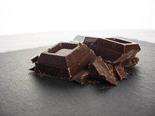 Pieces of broken chocolate bar. Sweet cocoa. Antioxidant food. Top view. Chocolate chunks on a dark slate background. Three pieces of chocolate, ingredient for recipe for dessert