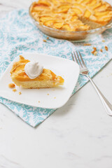 Homemade Peach Cake on a Turquoise and White Towel With One Slice on a White Plate with Dollop of Whipped Topping