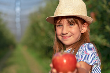 Beautiful Little Girl Giving Red Apple in Sunny Orchard