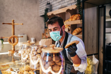Handsome middle age male worker with protective mask on face working in bakery.