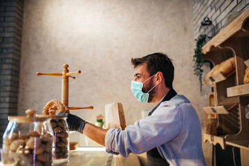 Handsome middle age male worker with protective mask on face working in bakery.