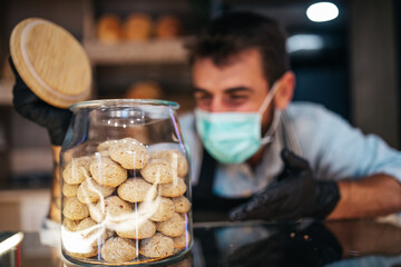 Handsome middle age male worker with protective mask on face working in bakery.
