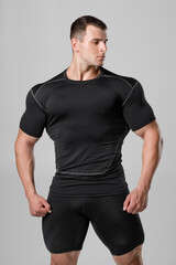 Muscular man in black compression sportswear on gray background