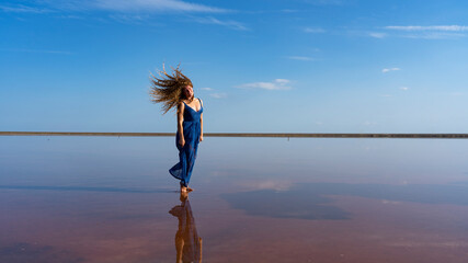 dreamy romantic girl walks along the shore in a blue long dress waving lush curly hair