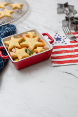 Pot Pie Made with Vegan Chicken Substitute Topped with Biscuts in a Star Shape; Red, White, Blue Napkins; Star Cookie Cutters on White Countertop