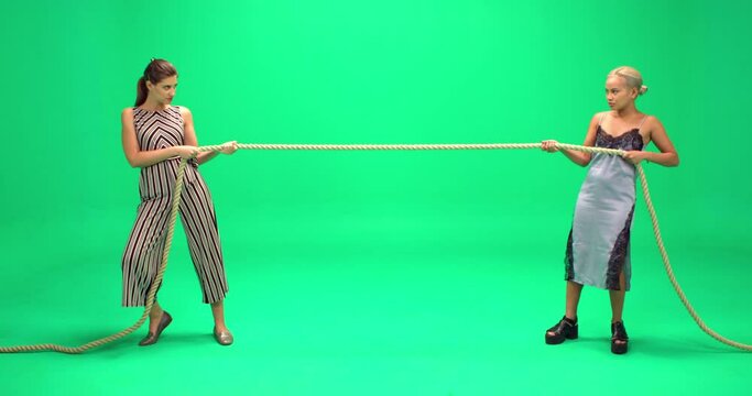 Studio, slow motion, two young women play tug of war against a green screen