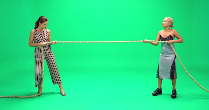 Studio, slow motion, two young women play tug of war against a green screen