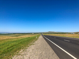 An empty highway on a summer sunny day against a background of blue sky and green hills. Travel by car.