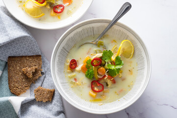 Rustic chicken soup with vegetables, noodles, lemon slice, celery leaves and fresh red chilli
