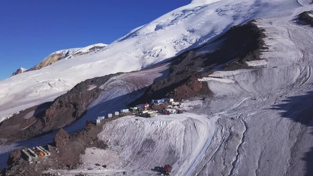 A row of houses built on a snowy mountain slope on blue sky background. Clip. Aerial view of garage buildings and machines located high in the mountains.