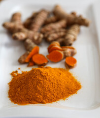 Turmeric as a whole root, sliced and ground into powder on white plate