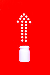 Arrow shape composed of white pills with a white plastic bottle on a red background