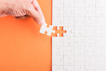 Top view flat lay of hand-holding last piece white paper jigsaw puzzle game last pieces put to...