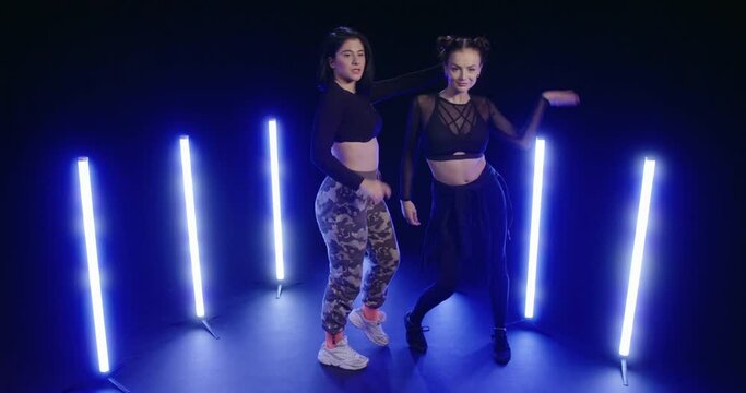 Studio, slow motion, two young women dancing backlit by ultraviolet light