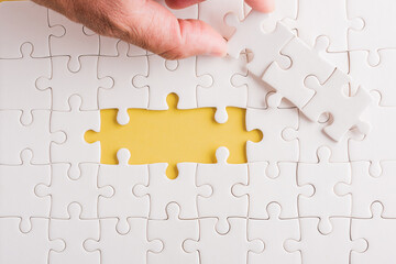 Fototapeta premium Top view flat lay of hand-holding last piece white paper jigsaw puzzle game last pieces put to place for solve problem complete mission, studio shot on a yellow background, quiz calculation concept