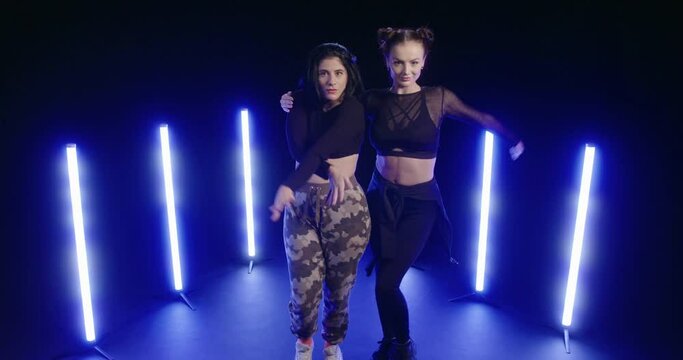 Studio, slow motion, two young women dancing backlit by ultraviolet light
