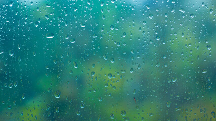 horizontal soft focused or blurred rainy window background. raindrops on the clear window glass, rainy day, blue and green background, evening light