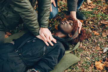 Guys help a woman. African girl is lying unconscious. Providing first aid in the park.