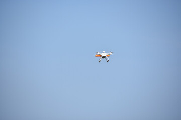 White ond orange drone flying  high in a blue sky
