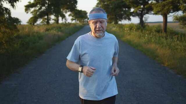 Bearded senior man in summer sports uniform running off the city touching smart watch to measure speed, distance and heart rate. Shot for graphic map hologram application. Wireless earphones. 4K